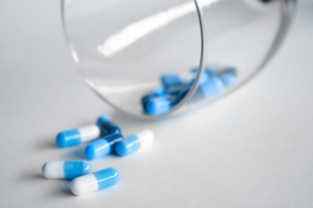 a glass with medication capsules spilling onto the table
